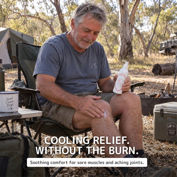 A man sitting in a folding camp chair outdoors in a wooded campsite setting, applying pure and natural pain relief cream from a white bottle to his knee. Text overlays read 'COOLING RELIEF.